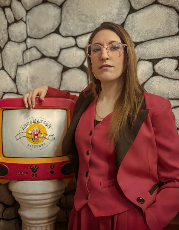 photo of the female director wearing a pink suit standing next to a TV set showing her film logo