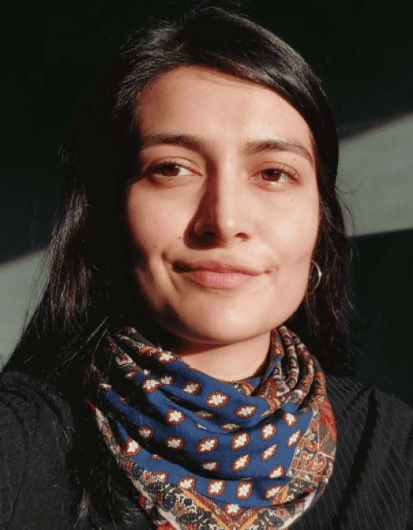 A mixed-race woman in her thirties with black hair stares intently at the camera, smiling slightly