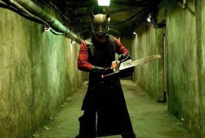 masked man with chainsaw stands in a hallway