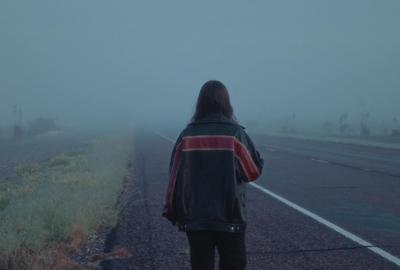 back of a woman in a jacket walking down a foggy highway