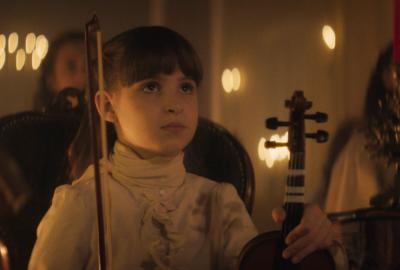 A little girl holds a violin looking on.