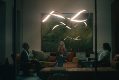 Three people sit in a modern living room with leather furniture and a unique light fixture