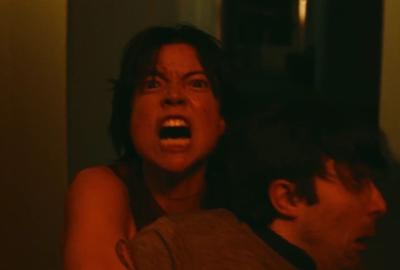 A woman screams while holding onto a man in a red glare