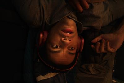 Reed (Miles Fowler) lays upside down wearing headphones, looking distressed.