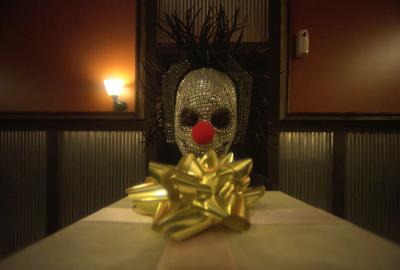 A clown mask looks at a gift with a bow