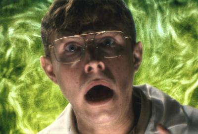 A scared man mid scream with green, swirling, flames behind him.