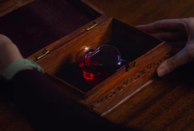 Hands open a wooden box with a heart shaped glass container of 
