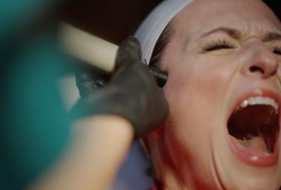 Close up of a young woman's face as she screams in great distress as a gloved hand holds a laser to her skin