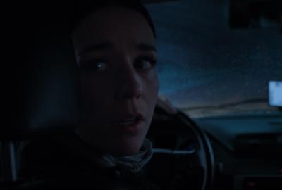 Frightened woman driving a car down a dark, snowy road, looking over her shoulder.