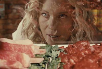 A woman stares at a selection of raw meat in a butcher case.