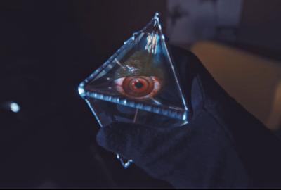 A gloved hand holds a mysterious object with an eye looking out