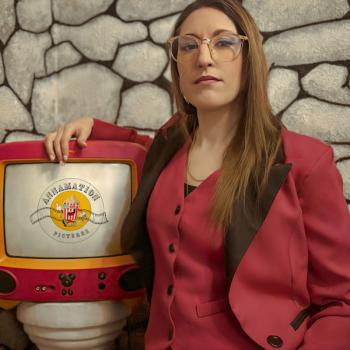 photo of the female director wearing a pink suit standing next to a TV set showing her film logo