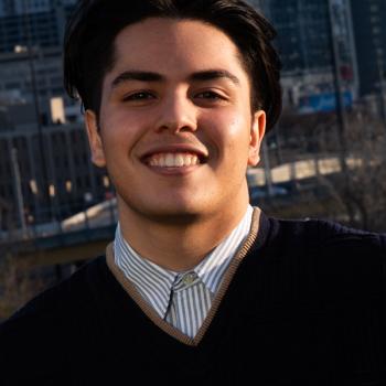 Man in a black vest with short black hair smiling.