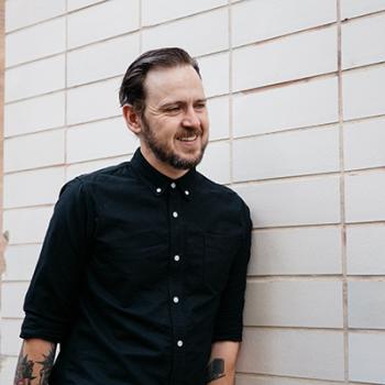 tony standing against a white wall smiling looking off camera